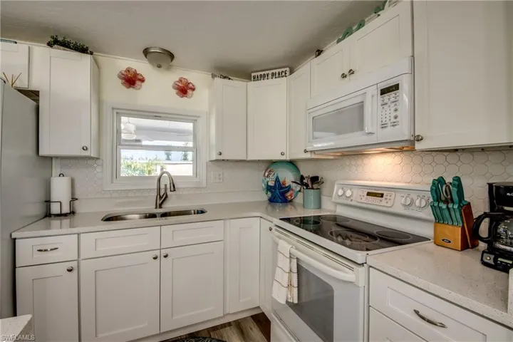 Kitchen featuring white appliances, white cabinetry, decorative backsplash, light stone countertops, and light wood-type flooring