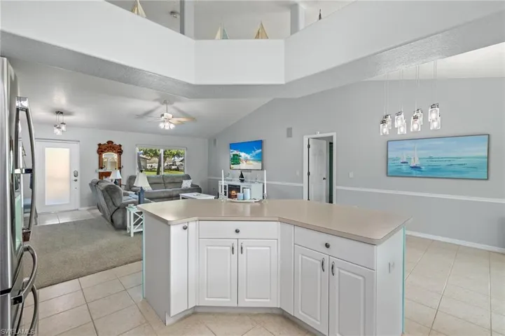 Kitchen featuring light tile flooring, ceiling fan, stainless steel fridge, white cabinets, and pendant lighting
