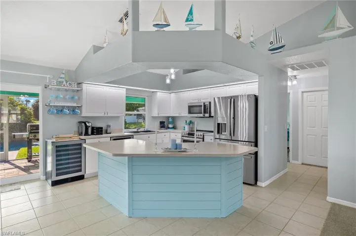 Kitchen with  stainless steel appliances, a center island with sink, track lighting, and hanging light fixtures