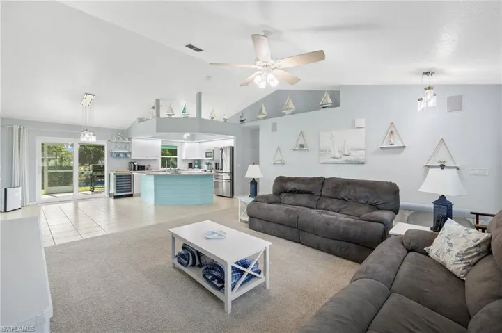 Living room featuring lofted ceiling, light tile floors, and ceiling fan with chandelier