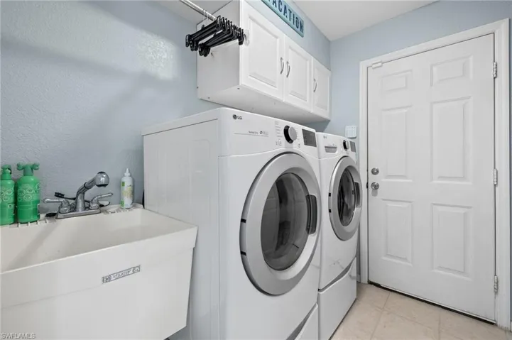 Laundry room with washer and clothes dryer, sink, light tile floors, and cabinets