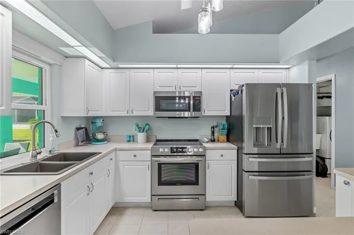 Kitchen with sink, stainless steel appliances, vaulted ceiling, and white cabinetry