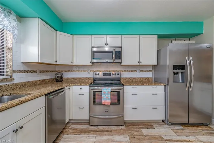 Kitchen featuring white cabinets, stone countertops, decorative backsplash, and appliances with stainless steel finishes