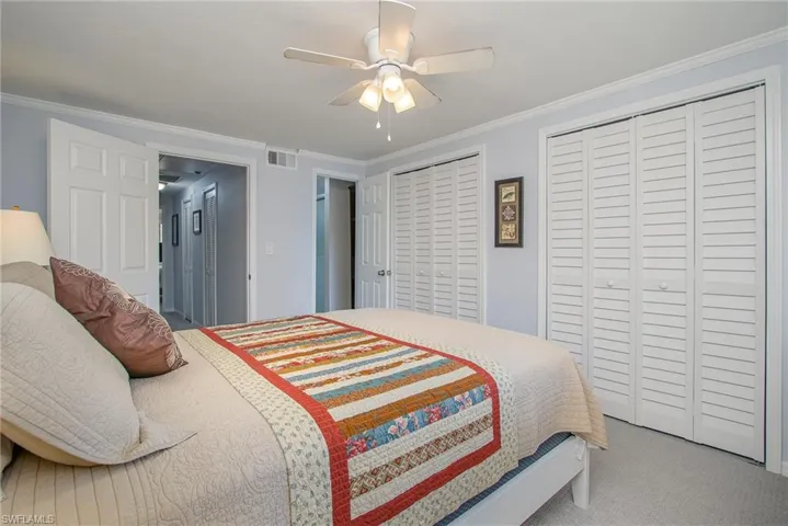 Bedroom with carpet flooring, two closets, ceiling fan, and crown molding