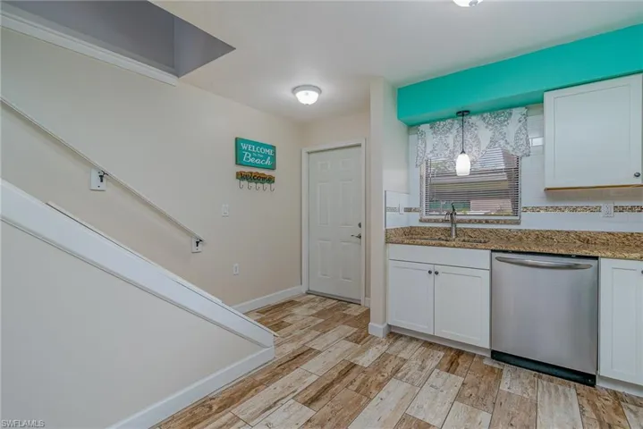 Kitchen featuring stainless steel dishwasher, decorative light fixtures, white cabinetry, and light hardwood / wood-style flooring