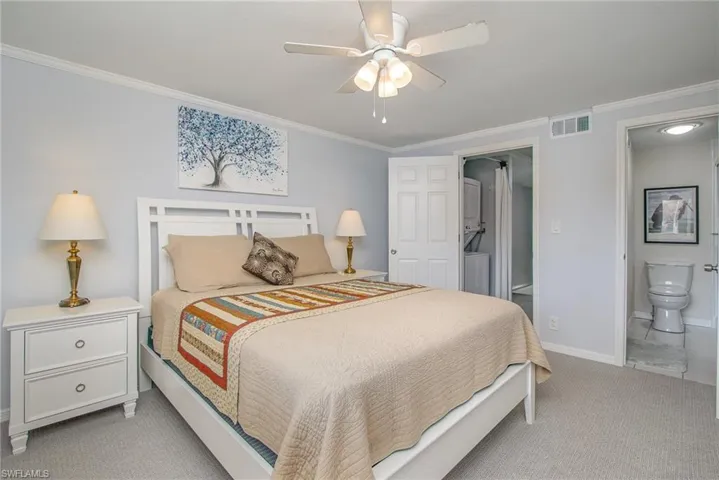 Bedroom with connected bathroom, ceiling fan, crown molding, and light carpet