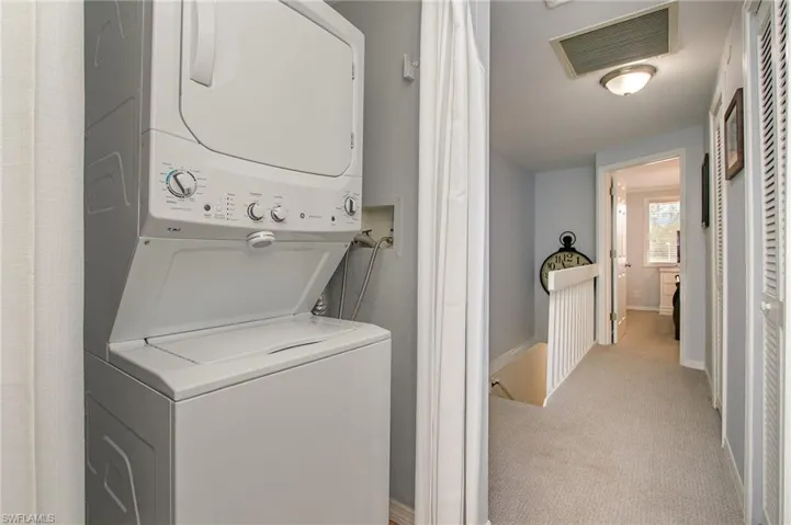 Laundry area featuring light colored carpet and stacked washer / dryer