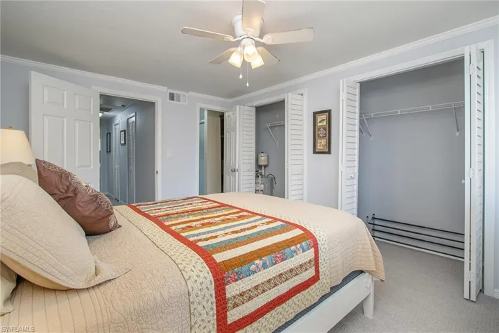 Carpeted bedroom featuring ornamental molding, ceiling fan, and multiple closets