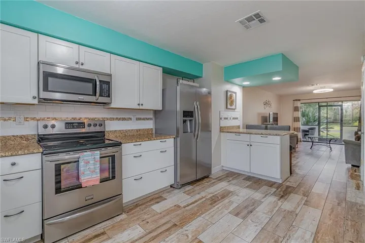 Kitchen with kitchen peninsula, stainless steel appliances, white cabinetry, and tasteful backsplash