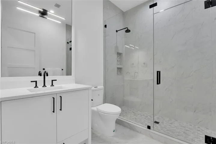 Full bath with a marble finish shower, marble look tile flooring, toilet, and vanity