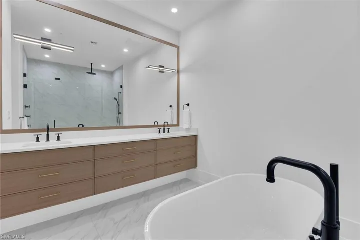 Full bath featuring marble finish floors, a marble finish shower, double vanity, recessed lighting, and a soaking tub