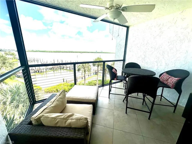 Expansive balcony with tiled flooring and a ceiling fan, offering views of the waterway and surrounding greenery