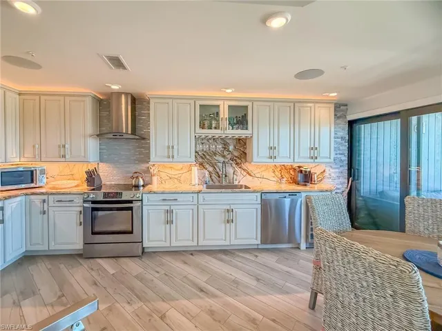 Kitchen with visible vents, decorative backsplash, stainless steel appliances, wall chimney exhaust hood, and a sink