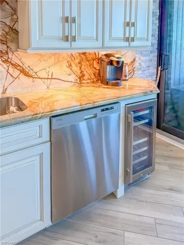 Bar with light wood-type flooring, wine cooler, decorative backsplash, bar, and dishwasher