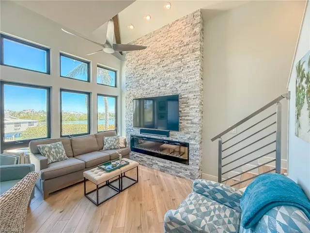 Living room with a stone fireplace, a high ceiling, a ceiling fan, and wood finished floors