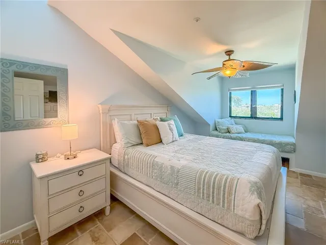 Bedroom featuring stone tile flooring, a ceiling fan, baseboards, and vaulted ceiling