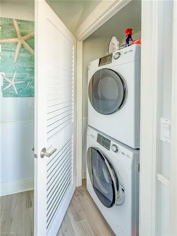 Laundry area with stacked washer and dryer and light wood-style floors