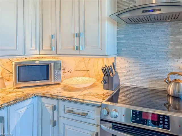 Kitchen featuring tasteful backsplash, appliances with stainless steel finishes, exhaust hood, white cabinets, and light stone countertops