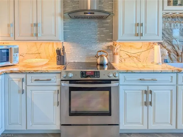 Kitchen featuring stainless steel appliances, white cabinetry, tasteful backsplash, and wall chimney range hood