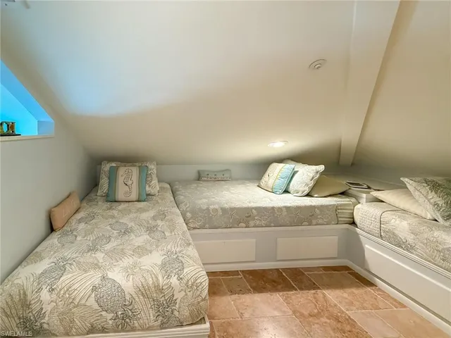 Unfurnished bedroom with vaulted ceiling and stone tile floors