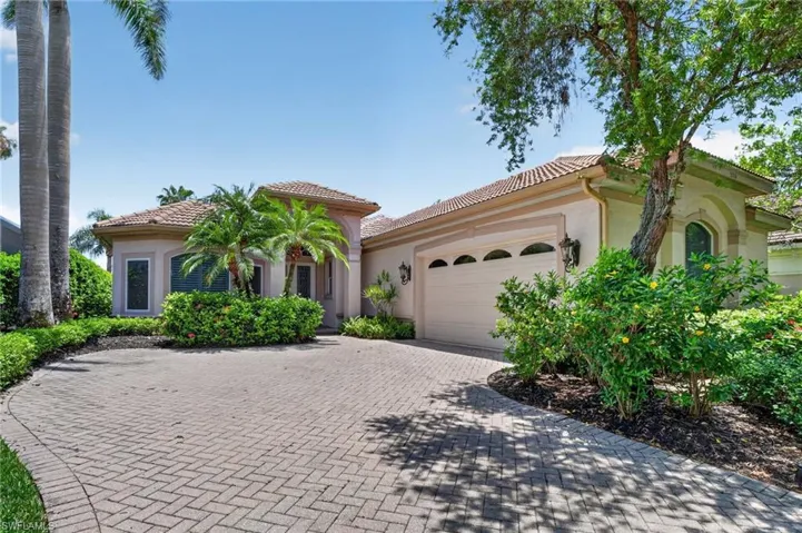 A paver driveway and mature trees frame the home.
