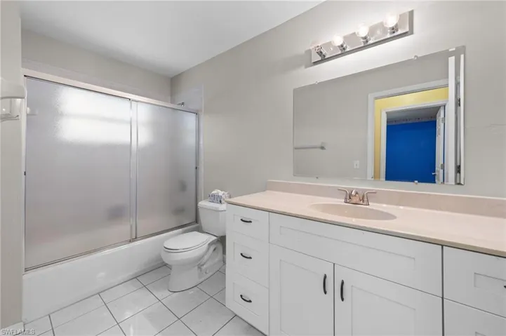 Bathroom with vanity, tile patterned flooring, toilet, and combined bath / shower with glass door