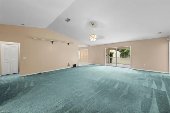 Carpeted spare room with a ceiling fan, vaulted ceiling, and baseboards