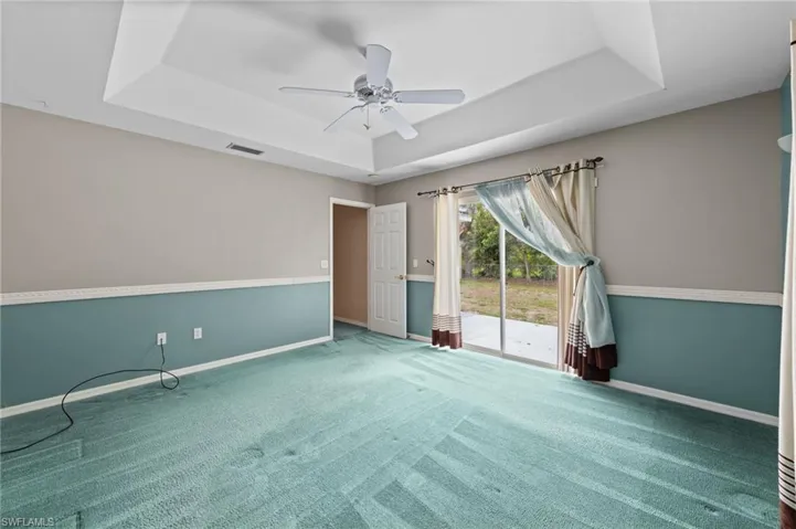 Carpeted spare room featuring a raised ceiling, baseboards, and ceiling fan
