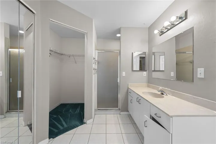 Bathroom with vanity, a shower stall, a walk in closet, tile patterned flooring, and baseboards