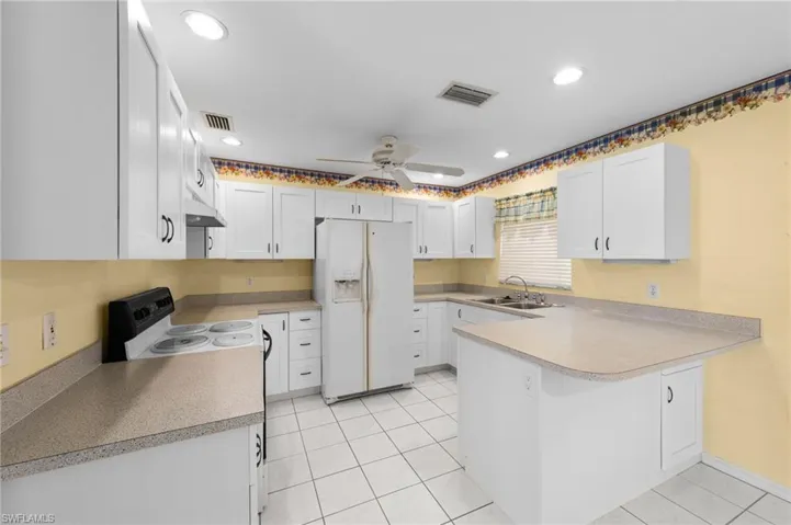 Kitchen featuring white appliances, a sink, a peninsula, ceiling fan, and light countertops