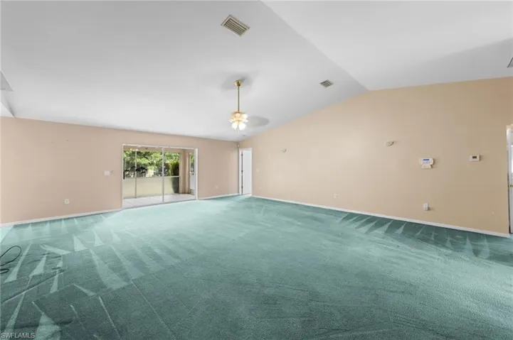 Empty room featuring lofted ceiling, ceiling fan, carpet floors, and baseboards