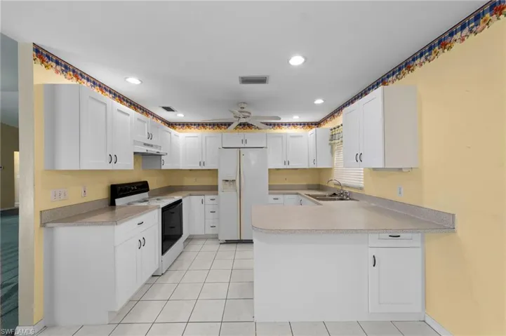 Kitchen with range with electric cooktop, under cabinet range hood, white refrigerator with ice dispenser, a sink, and a peninsula
