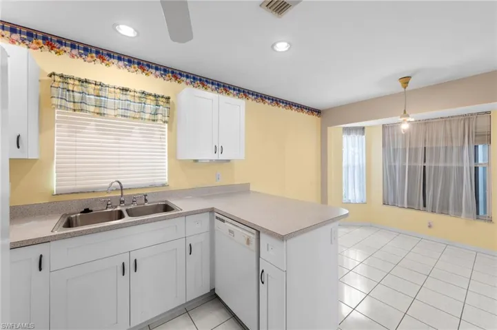 Kitchen featuring dishwasher, a sink, a peninsula, white cabinetry, and light countertops