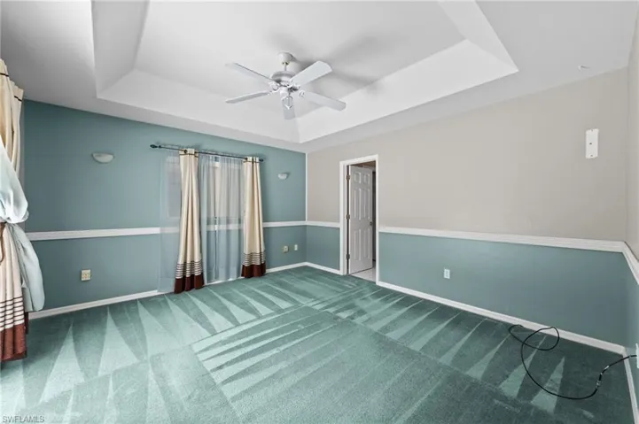 Unfurnished bedroom featuring a raised ceiling, carpet floors, baseboards, and a ceiling fan
