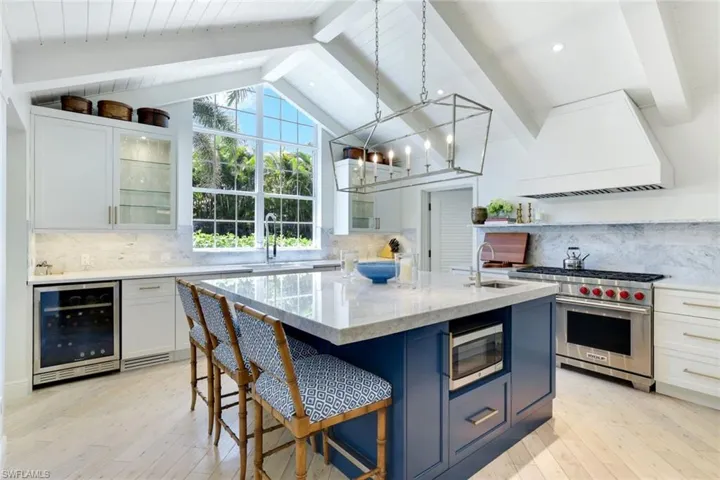Kitchen featuring backsplash, beverage cooler, white cabinetry, and light stone counters