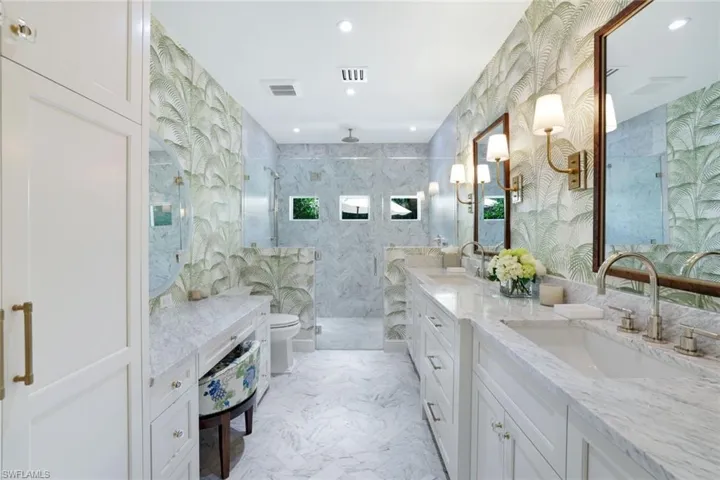 Full bathroom featuring double vanity, a marble finish shower, light marble finish floors, recessed lighting, and tile walls