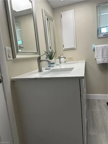 Dual vanity with integrated sinks and satin nickel faucets, framed mirrors, recessed medicine cabinet, and wood-finish tile flooring