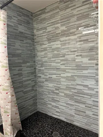 Shower enclosure featuring linear mosaic wall tile in varying shades of gray, dark pebble-finish flooring, and a visible floor drain