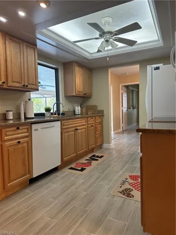 Kitchen featuring wood cabinetry, light-toned countertops, a white dishwasher, and light plank flooring