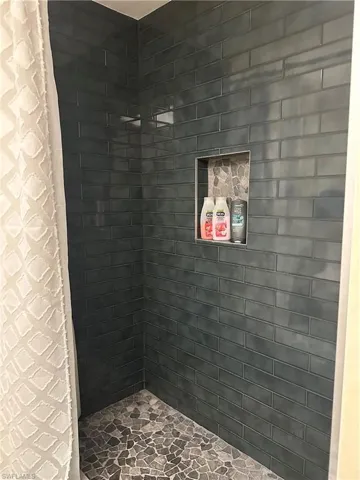 Shower stall with dark subway tile walls, a built-in recessed niche featuring mosaic tile backing, and a dark pebble tile floor