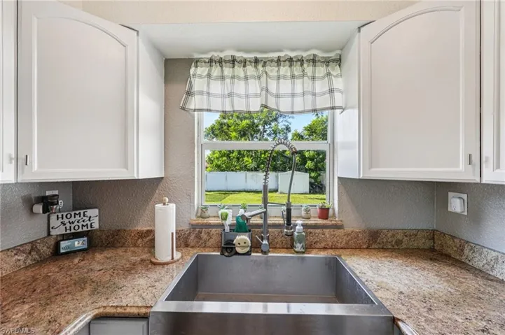 Kitchen featuring a textured wall, dark stone counters, and white cabinetry