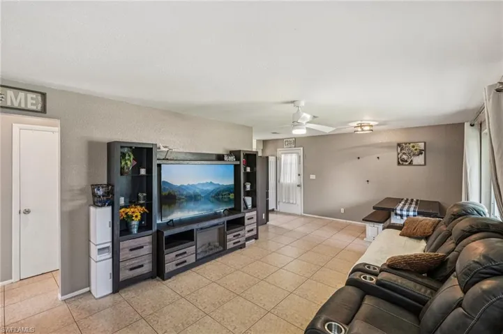 Living room with a textured wall, light tile patterned floors, and a ceiling fan
