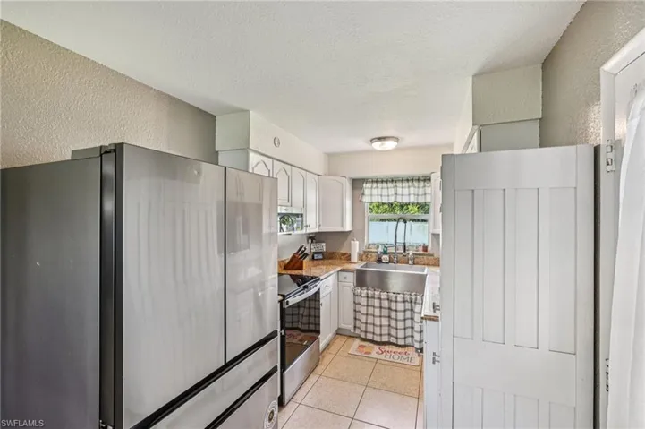 Kitchen with a textured wall, appliances with stainless steel finishes, light countertops, white cabinetry, and a textured ceiling