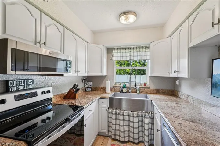 Kitchen featuring a textured wall, stainless steel appliances, a textured ceiling, white cabinets, and light stone counters