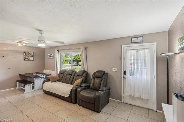 Living room featuring a textured wall, a textured ceiling, ceiling fan, and light tile patterned floors