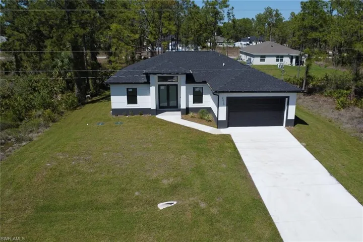 View of front of property featuring a front yard, concrete driveway, a garage, stucco siding, and a shingled roof
