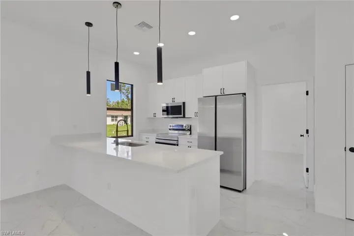 Kitchen featuring white cabinets, stainless steel appliances, quartz countertops, and hanging light fixtures