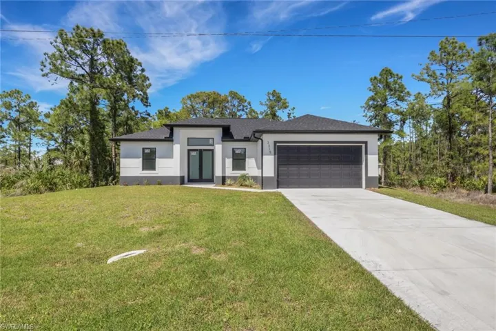 View of front of house with an attached garage, a front lawn, concrete driveway, and stucco siding