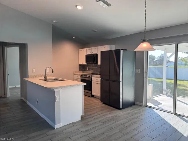 Kitchen featuring appliances with stainless steel finishes, light countertops, decorative backsplash, white cabinets, and a peninsula