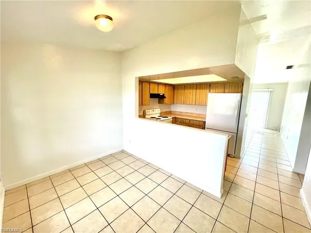 Kitchen featuring brown cabinetry, freestanding refrigerator, light countertops, white electric range oven, and a peninsula